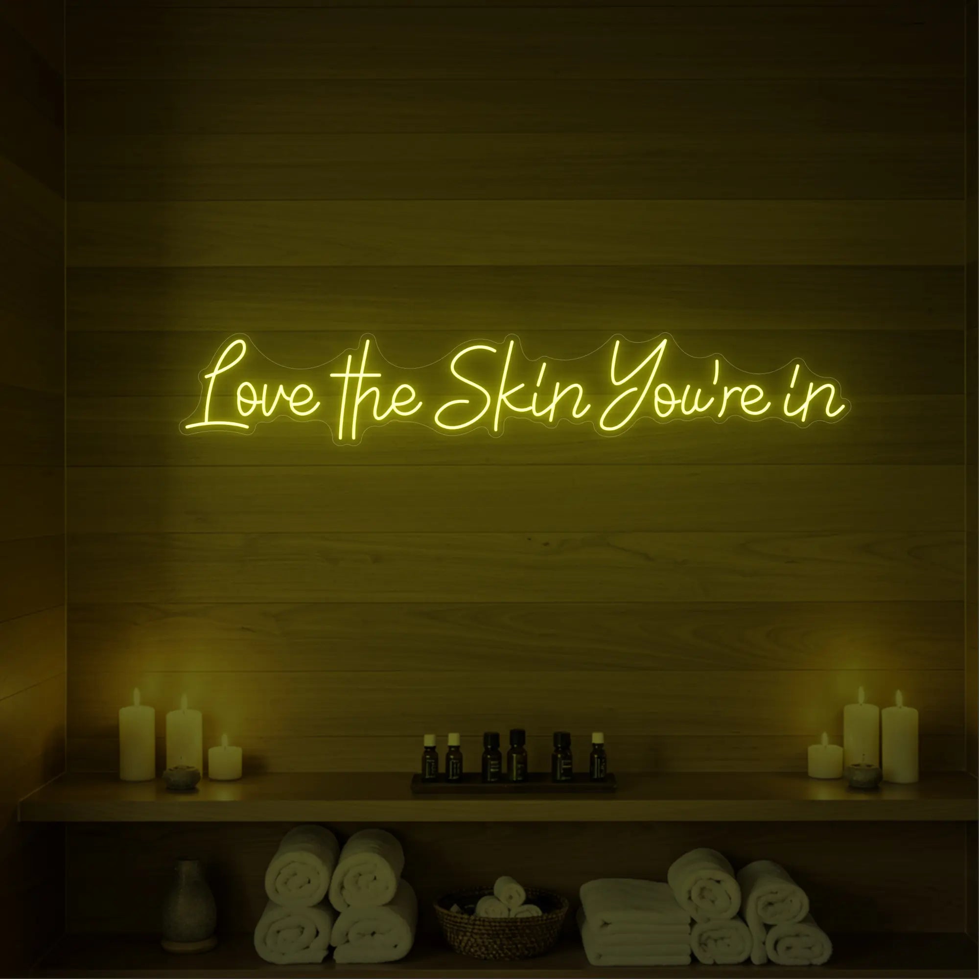 Photo of the 'Love the Skin You're In' neon sign glowing in lemon yellow against a styled interior wall.