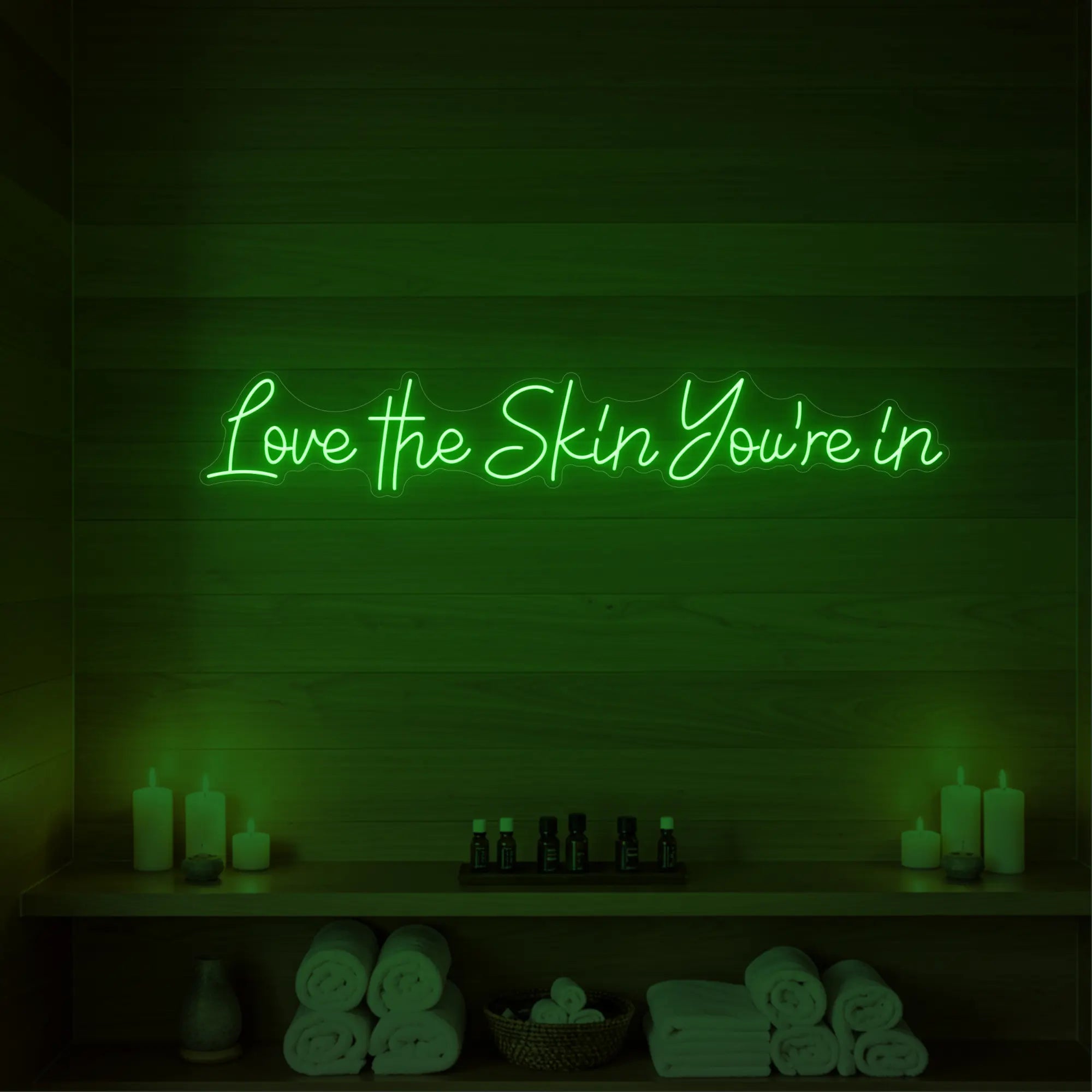 Photo of the 'Love the Skin You're In' neon sign glowing in green against a styled interior wall.