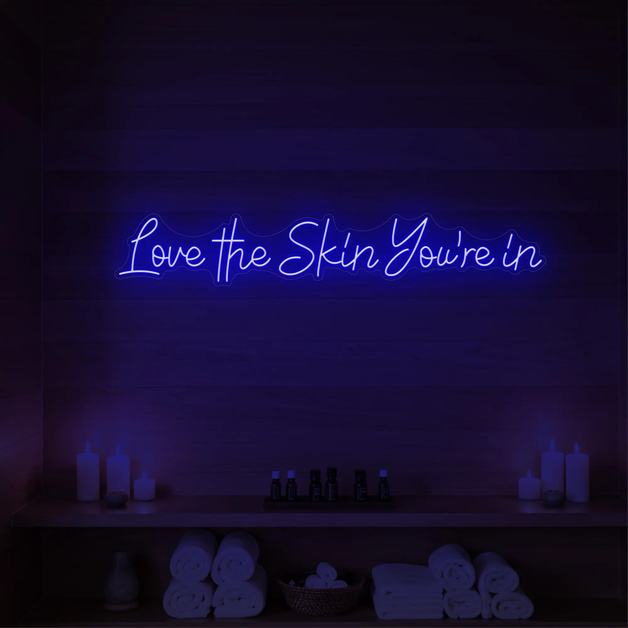 Photo of the 'Love the Skin You're In' neon sign glowing in deep blue against a styled interior wall.