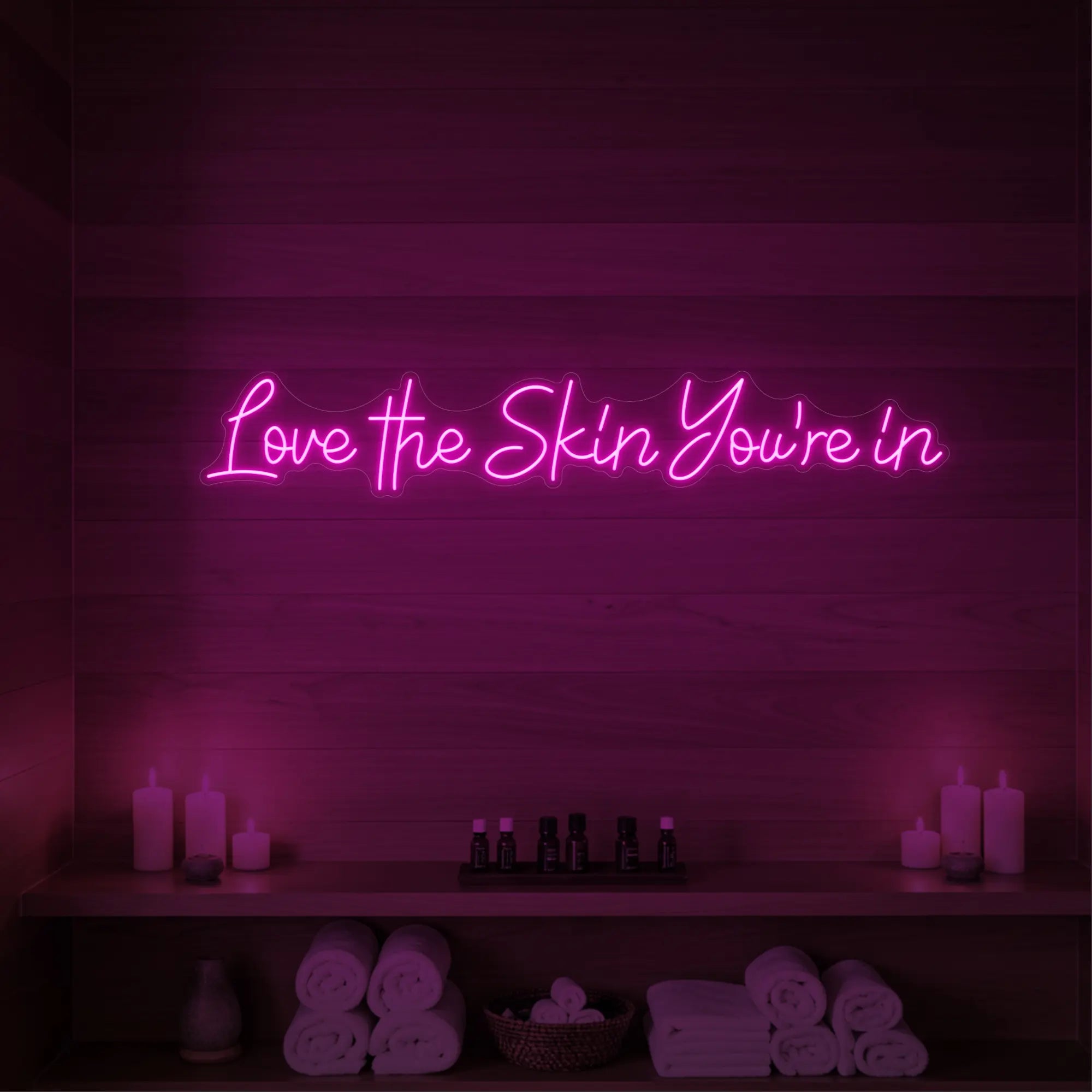 Photo of the 'Love the Skin You're In' neon sign glowing in light pink against a styled interior wall.