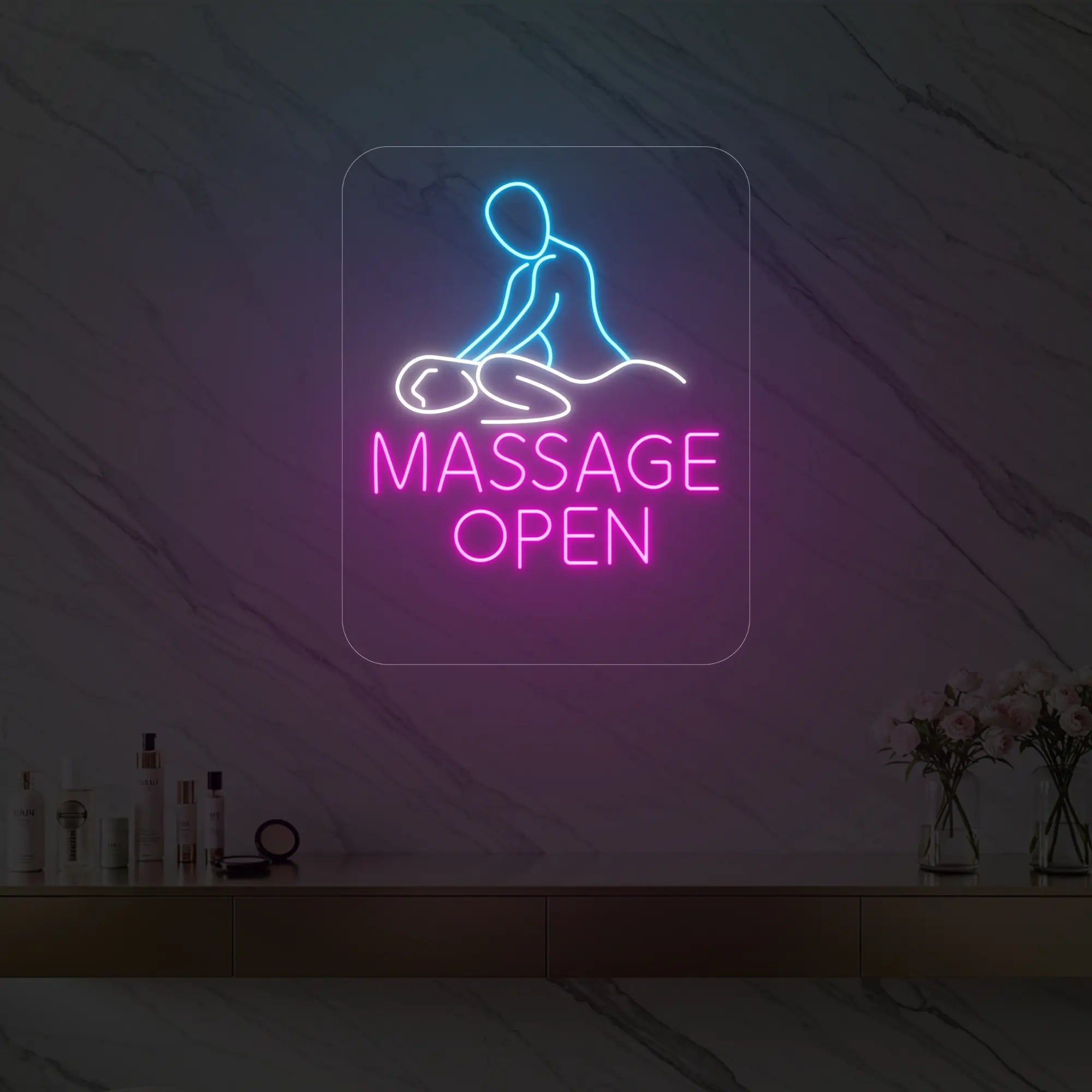 Photo of the 'Massage Open' neon sign glowing in cool white, pink and ice blue against a styled interior wall.