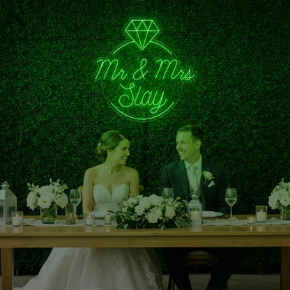 Photo of the 'Mr & Mrs EST' neon sign glowing in green against a styled interior wall.
