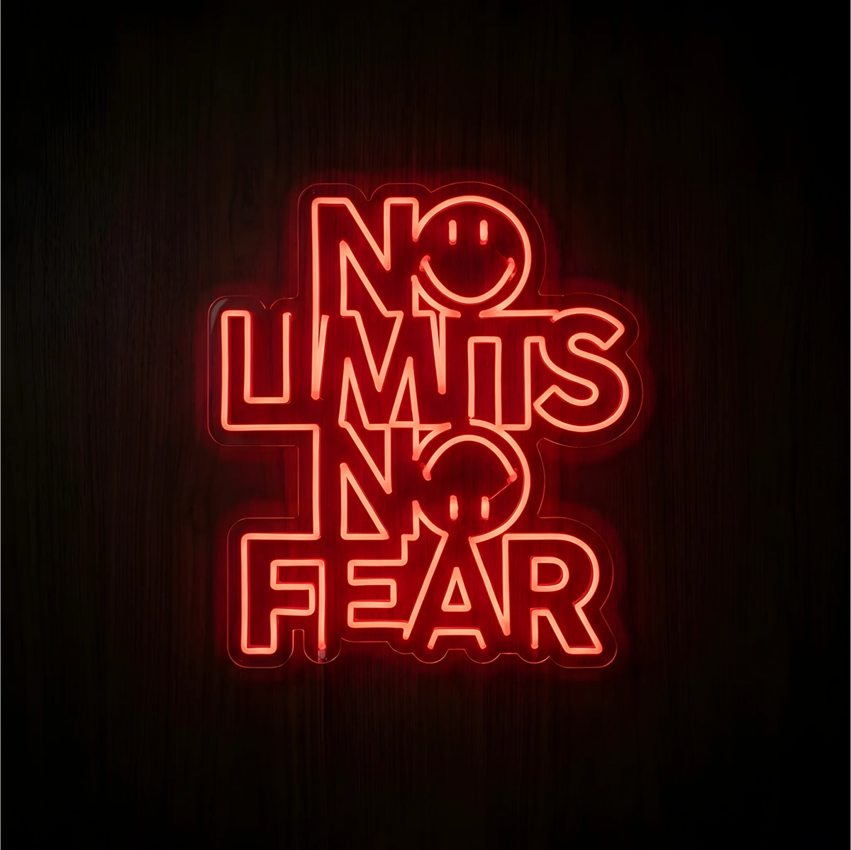 “No Limits No Fear” LED Neon Sign glowing red-orange, with two smiling face designs integrated into the lettering, on clear acrylic against a dark wood background, suited to gyms and motivational workspaces.
