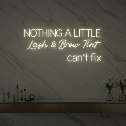 Photo of the 'Nothing a Little Lash & Brow Tint Can’t Fix' neon sign glowing in warm white against a styled interior wall.