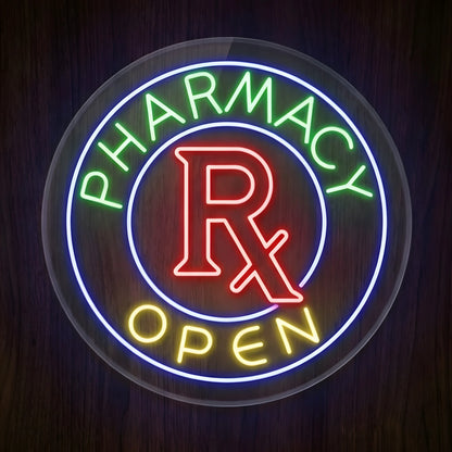 Pharmacy Rx Open LED Neon Sign featuring green PHARMACY text, red Rx symbol, yellow OPEN lettering, and a glowing blue circular border on clear round acrylic against a dark wooden wall.