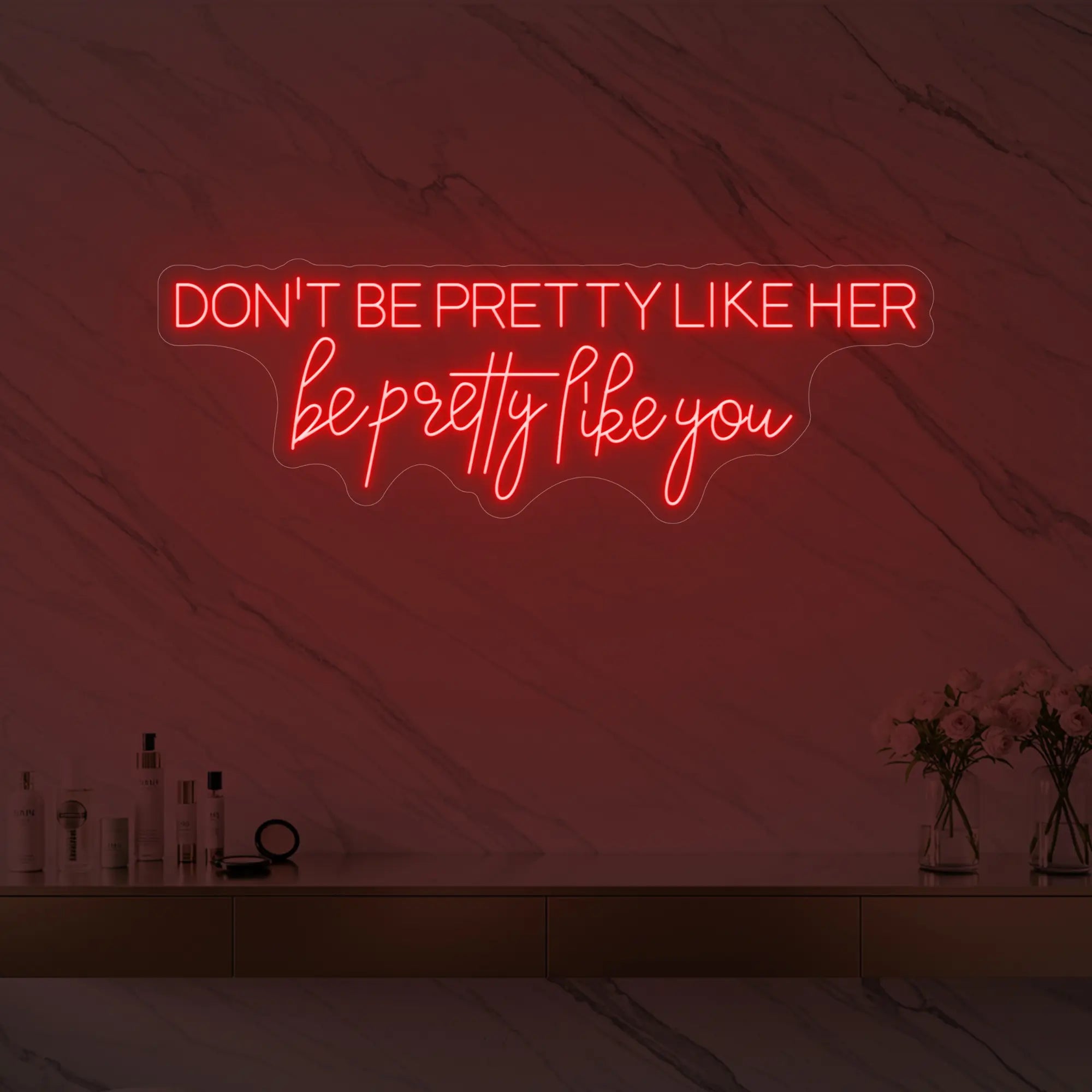 Photo of the 'DON'T BE PRETTY LIKE HER — be pretty like you' neon sign glowing in red against a styled interior wall.