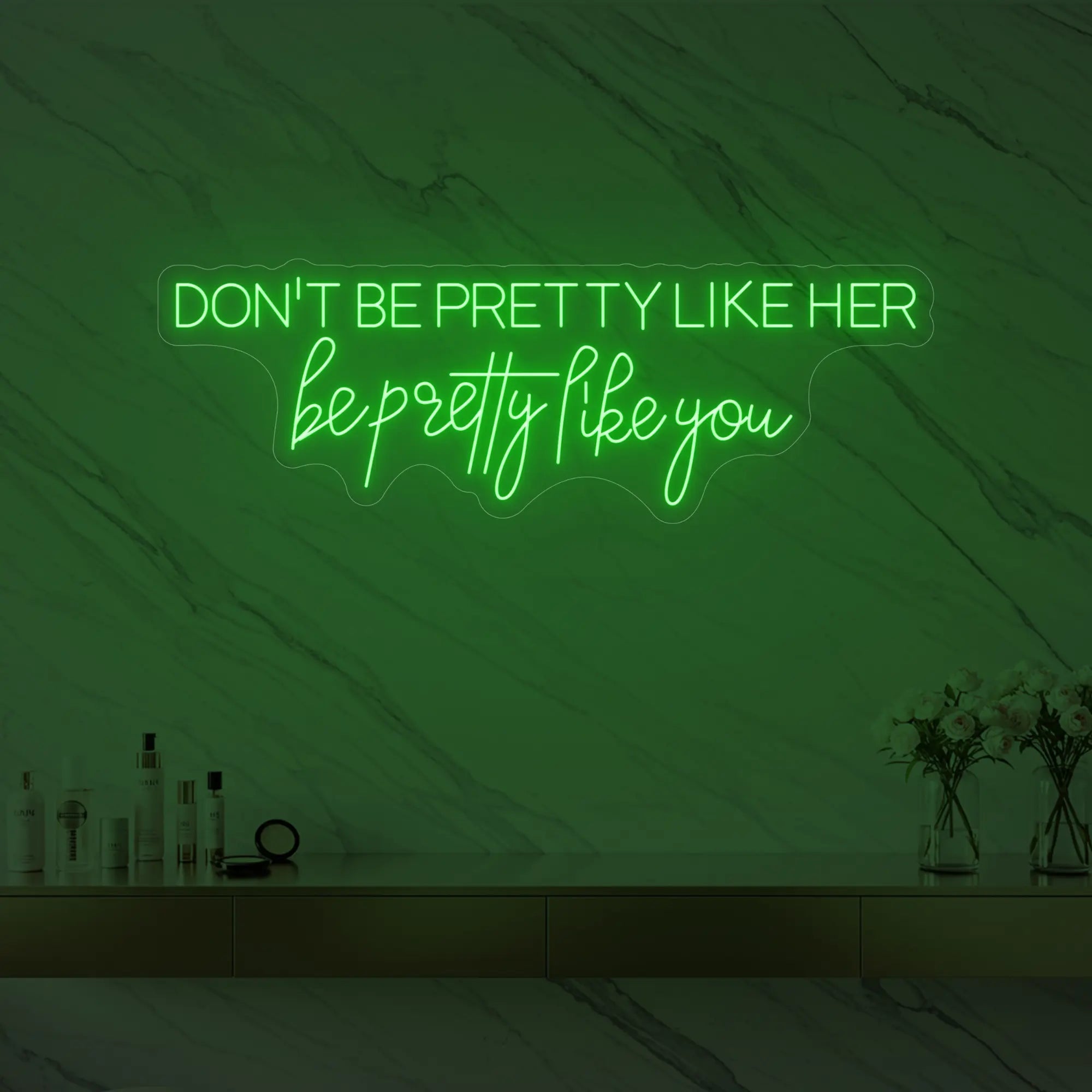 Photo of the 'DON'T BE PRETTY LIKE HER — be pretty like you' neon sign glowing in green against a styled interior wall.