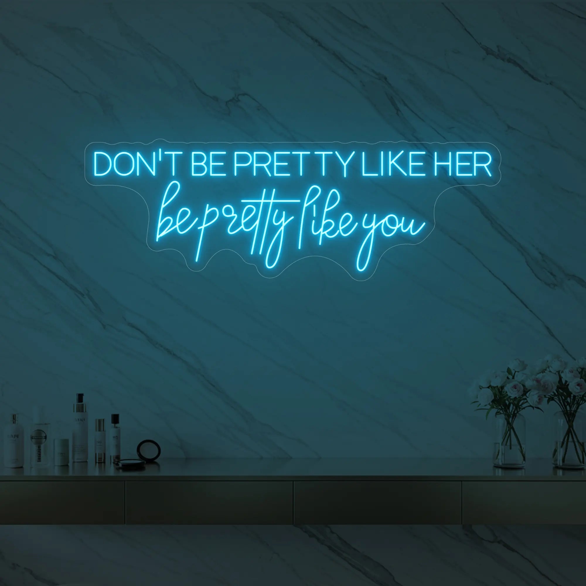 Photo of the 'DON'T BE PRETTY LIKE HER — be pretty like you' neon sign glowing in ice blue against a styled interior wall.
