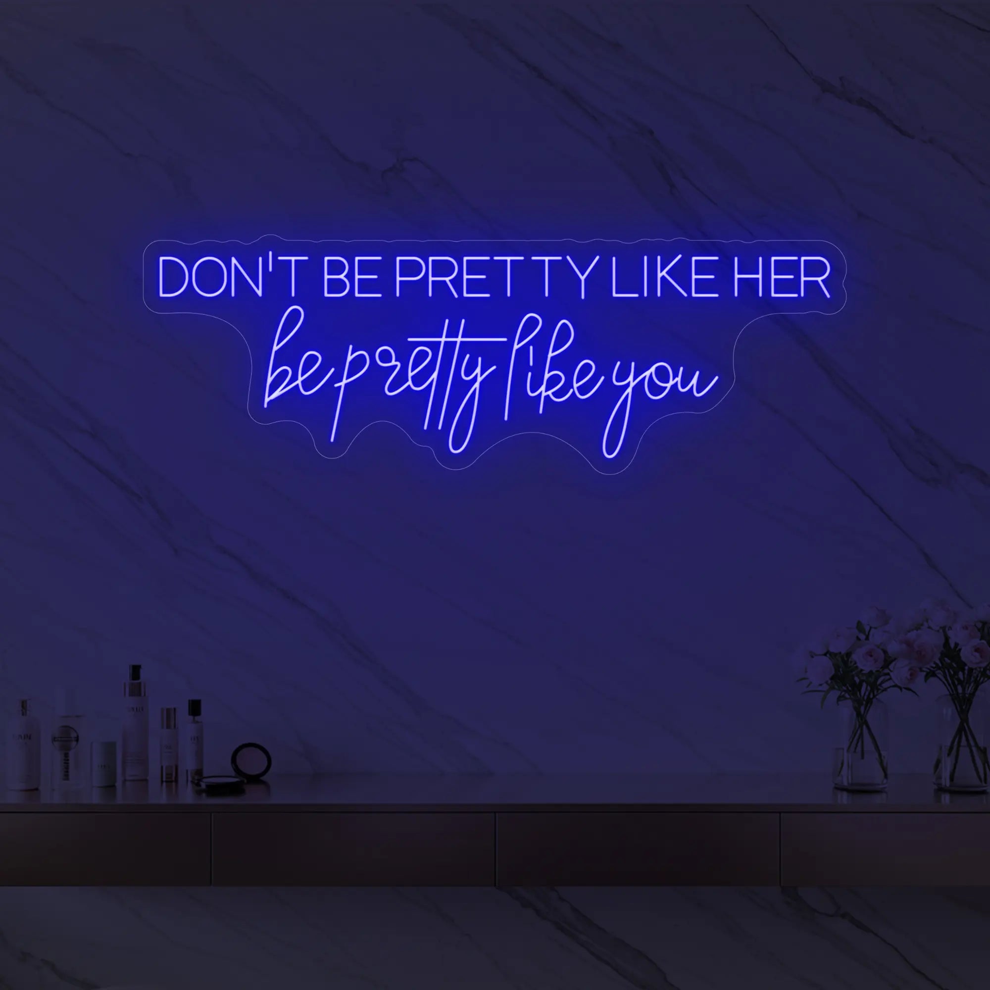 Photo of the 'DON'T BE PRETTY LIKE HER — be pretty like you' neon sign glowing in deep blue against a styled interior wall.