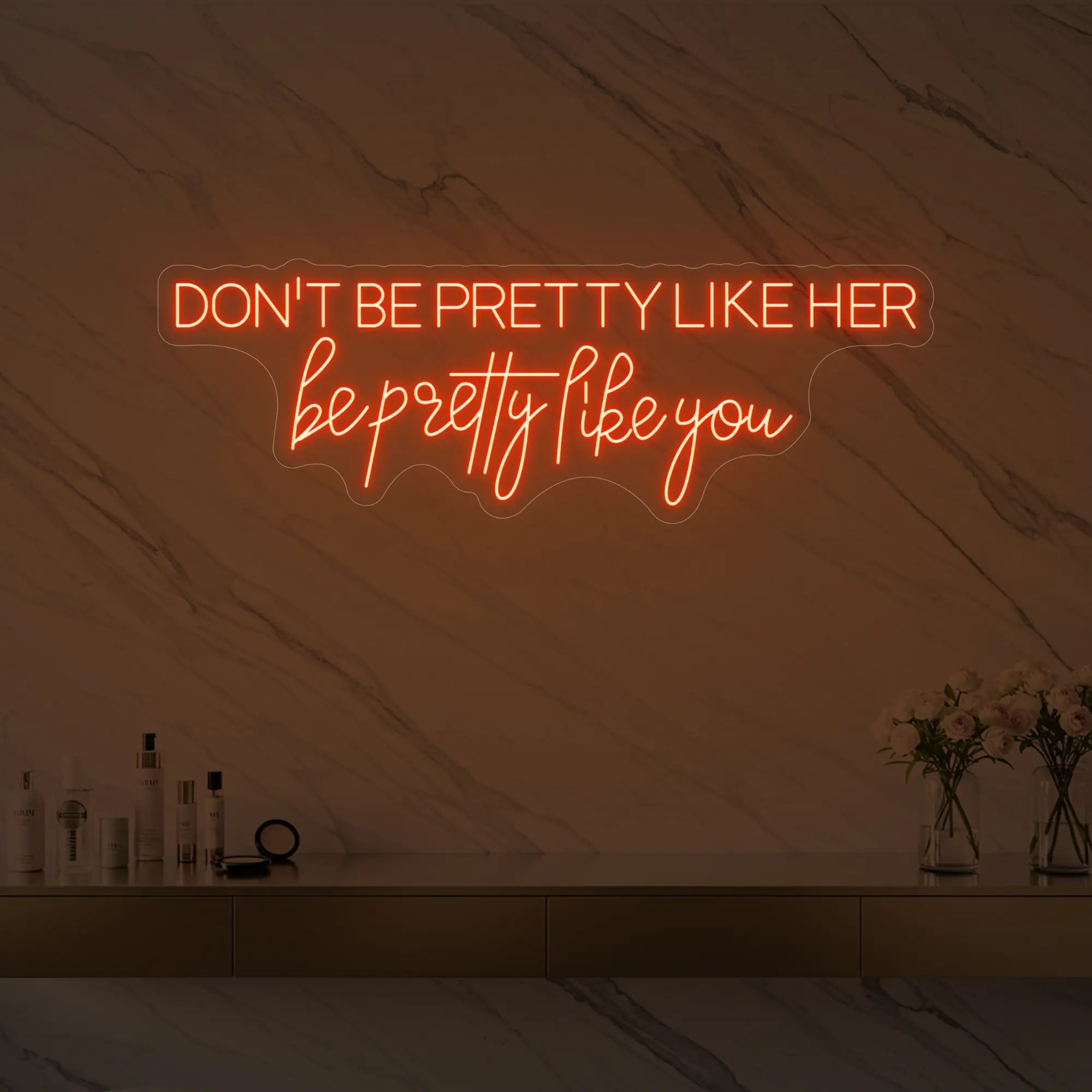 Photo of the 'DON'T BE PRETTY LIKE HER — be pretty like you' neon sign glowing in golden yellow against a styled interior wall.