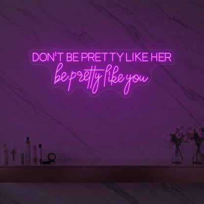 Photo of the 'DON'T BE PRETTY LIKE HER — be pretty like you' neon sign glowing in deep pink against a styled interior wall.