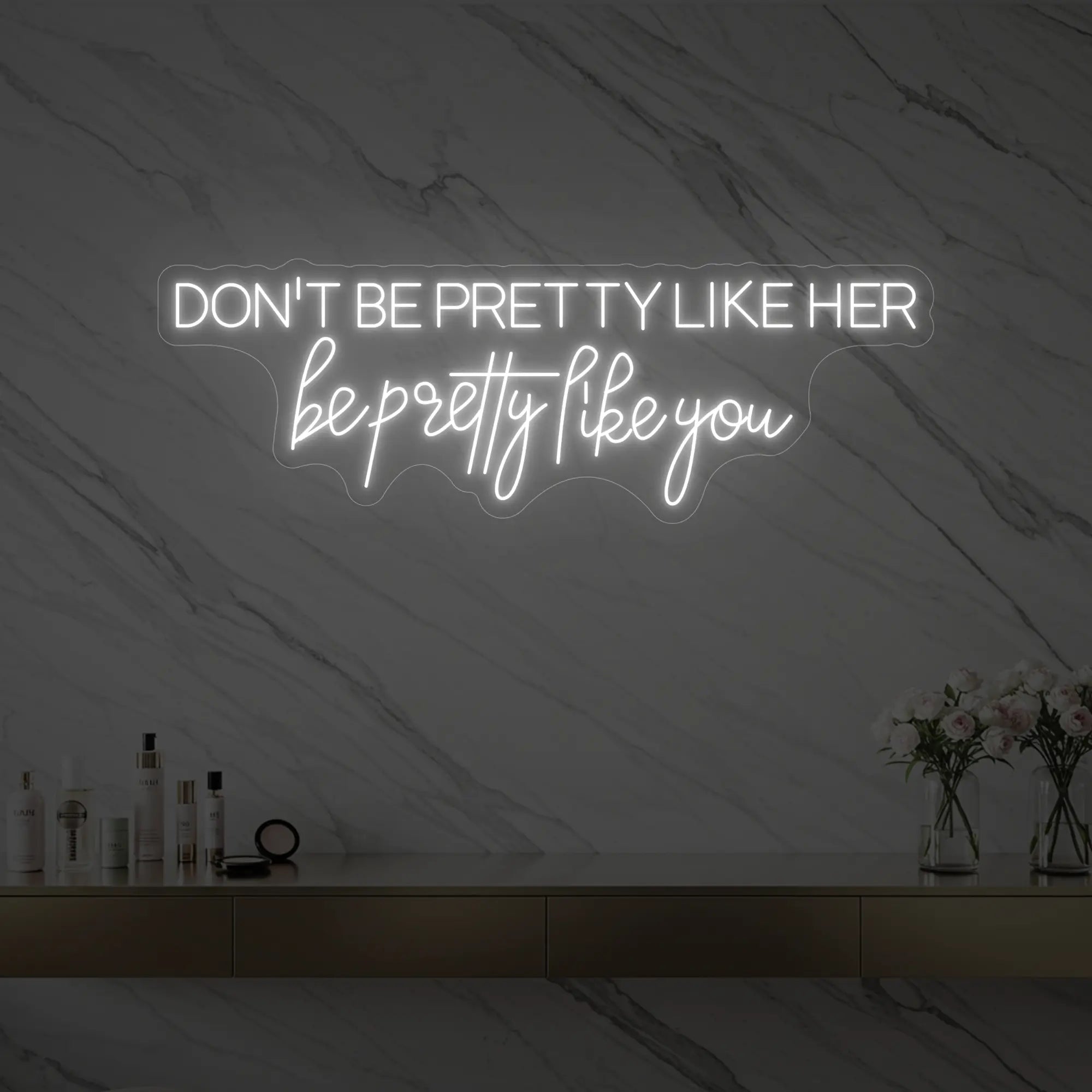 Photo of the 'DON'T BE PRETTY LIKE HER — be pretty like you' neon sign glowing in cool white against a styled interior wall.