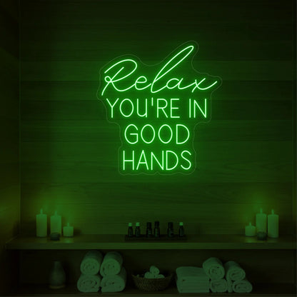 Photo of the 'Relax You're in Good Hands' neon sign glowing in green against a styled interior wall.