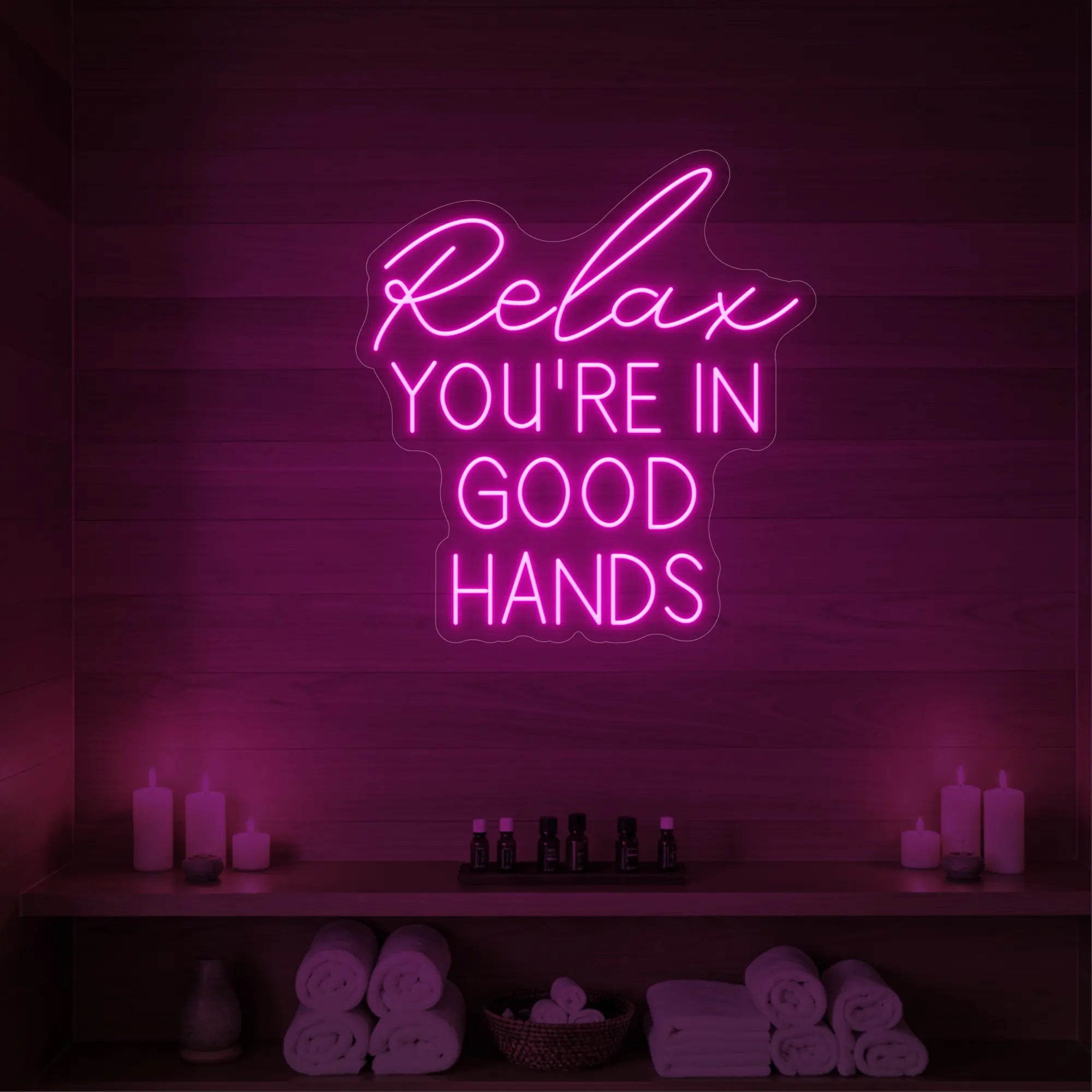 Photo of the 'Relax You're in Good Hands' neon sign glowing in light pink against a styled interior wall.