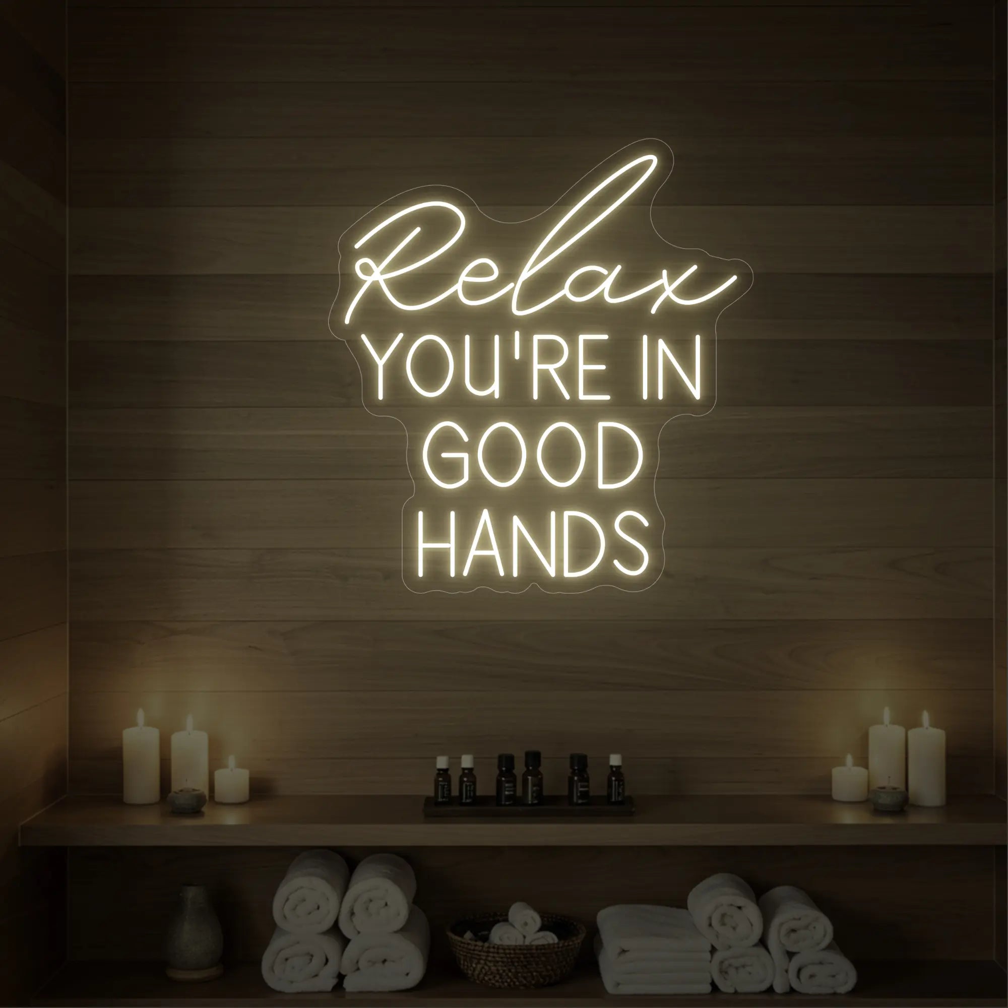 Photo of the 'Relax You're in Good Hands' neon sign glowing in warm white against a styled interior wall.