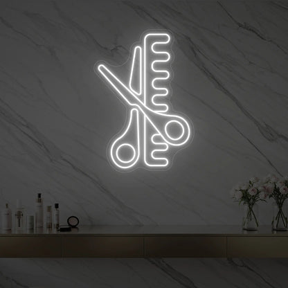 Photo of the 'Scissors and Comb' neon sign glowing in cool white against a styled interior wall.