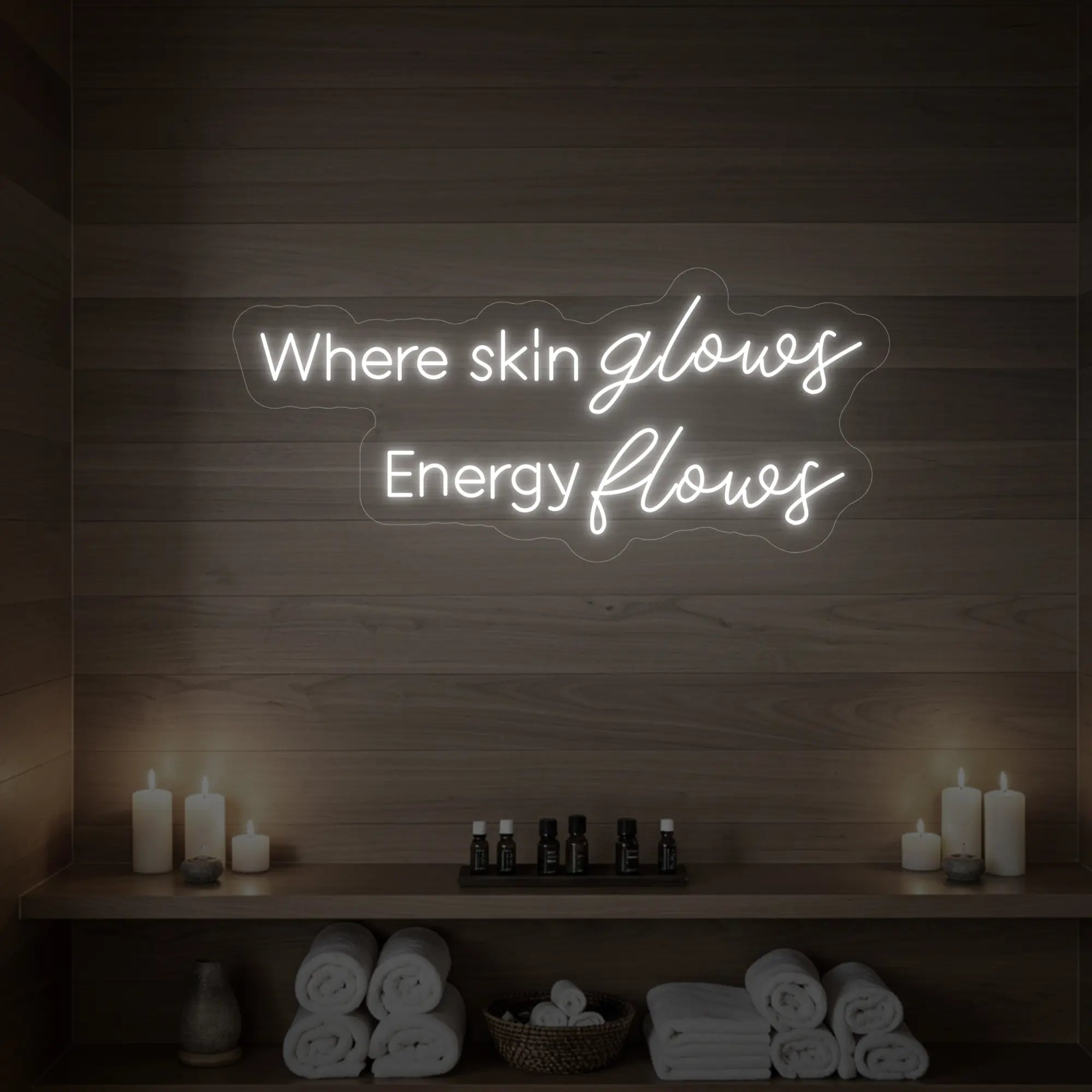 Photo of the 'Where Skin Glows, Energy Flows' neon sign glowing in cool white against a styled interior wall.