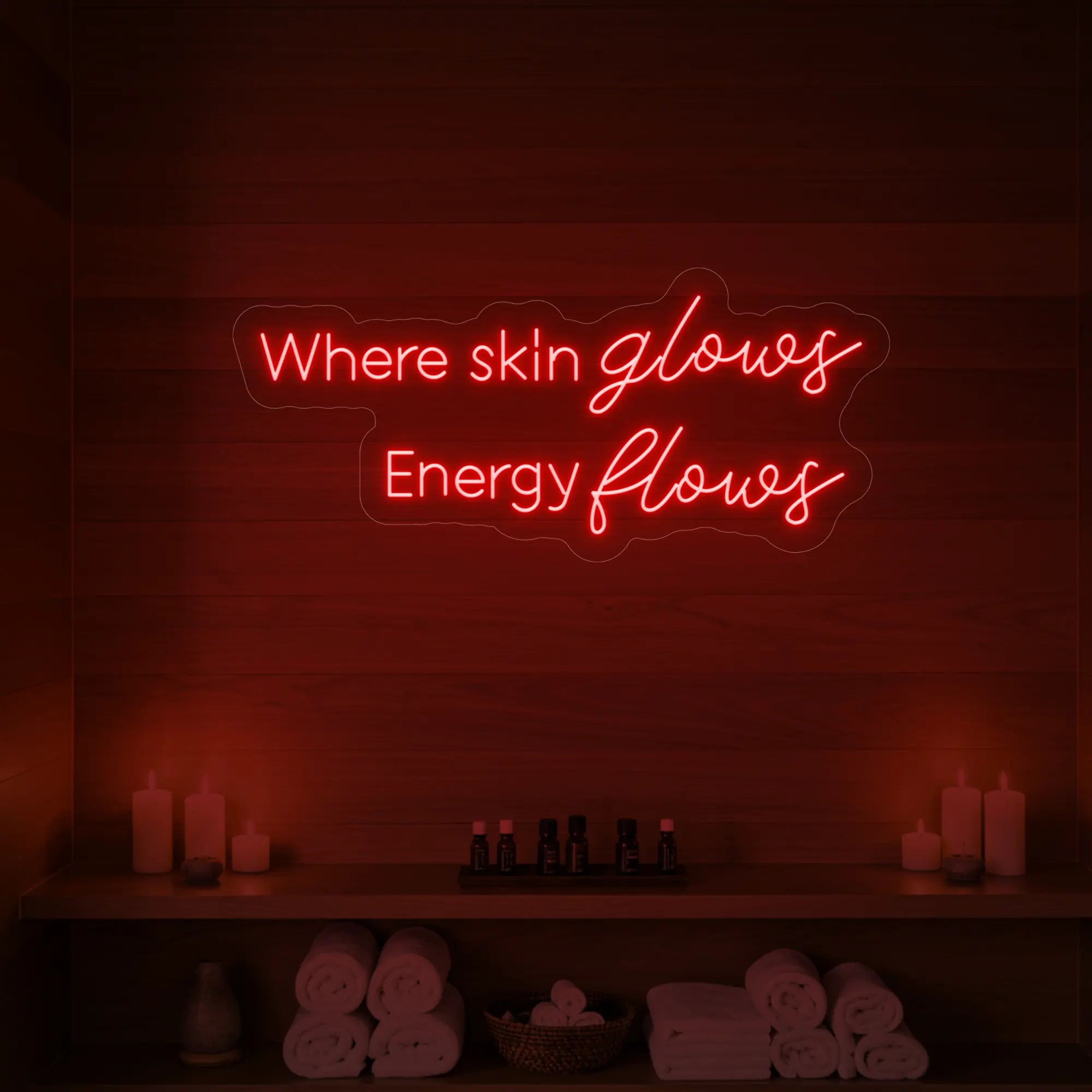 Photo of the 'Where Skin Glows, Energy Flows' neon sign glowing in red against a styled interior wall.