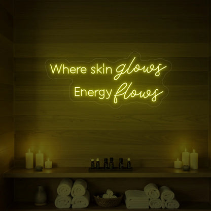 Photo of the 'Where Skin Glows, Energy Flows' neon sign glowing in lemon yellow against a styled interior wall.