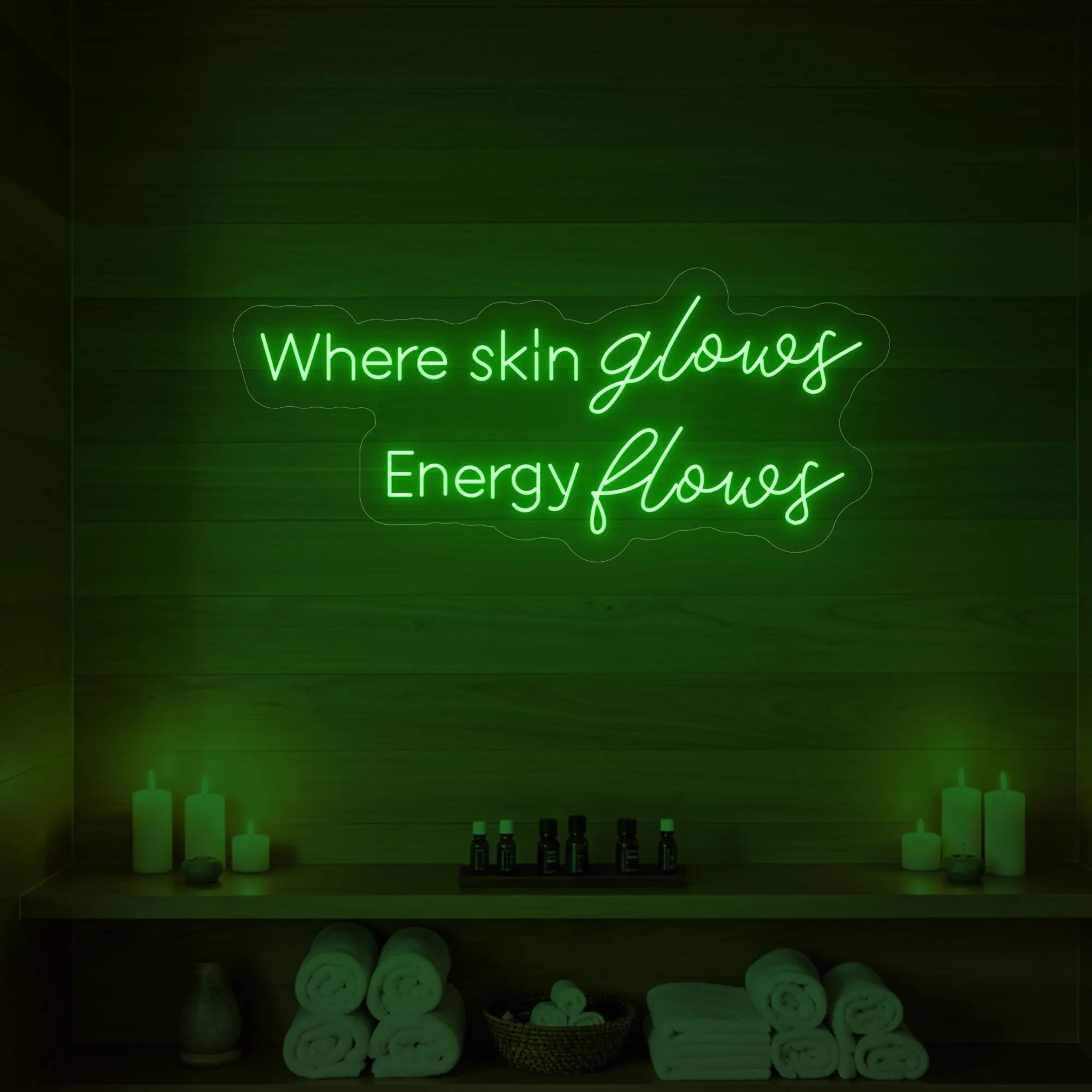 Photo of the 'Where Skin Glows, Energy Flows' neon sign glowing in green against a styled interior wall.