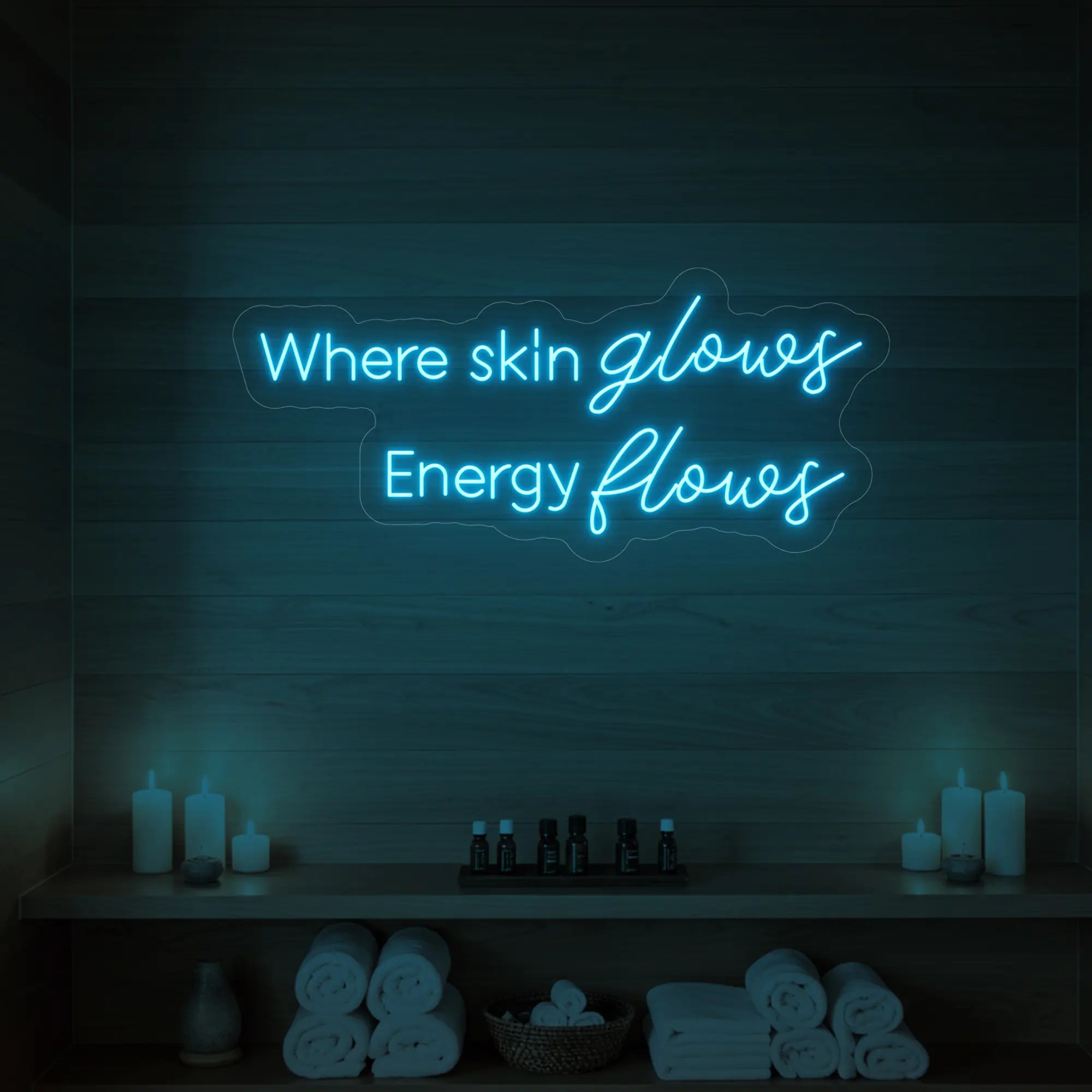 Photo of the 'Where Skin Glows, Energy Flows' neon sign glowing in ice blue against a styled interior wall.