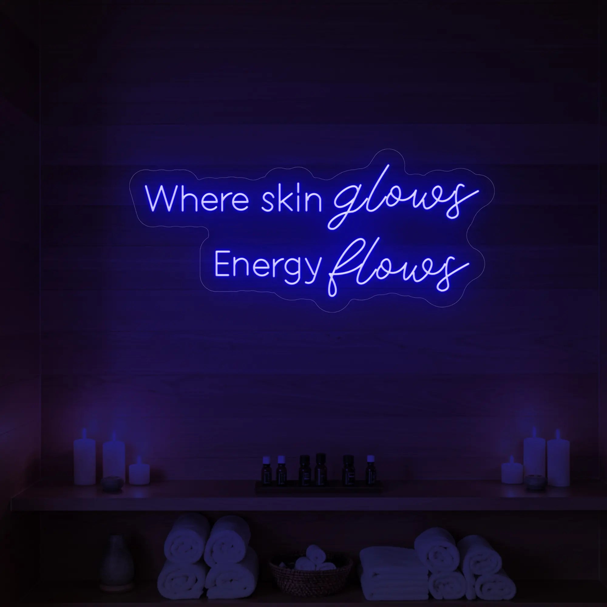 Photo of the 'Where Skin Glows, Energy Flows' neon sign glowing in deep blue against a styled interior wall.
