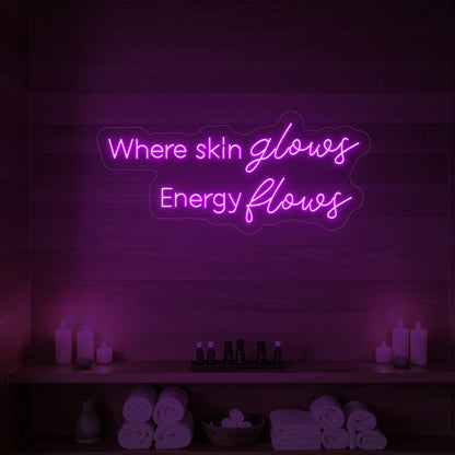 Photo of the 'Where Skin Glows, Energy Flows' neon sign glowing in deep pink against a styled interior wall.