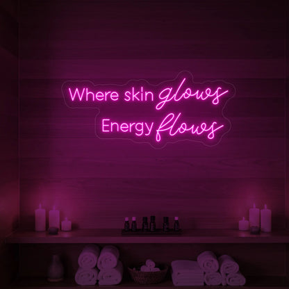 Photo of the 'Where Skin Glows, Energy Flows' neon sign glowing in light pink against a styled interior wall.