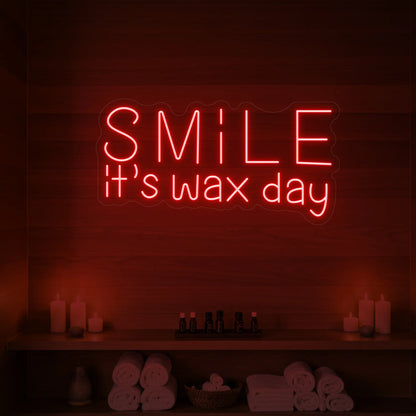 Photo of the 'Smile It’s Wax Day' neon sign glowing in red against a styled interior wall.