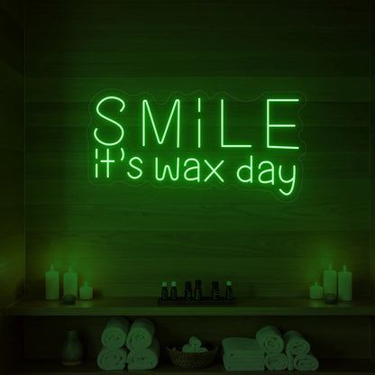 Photo of the 'Smile It’s Wax Day' neon sign glowing in green against a styled interior wall.