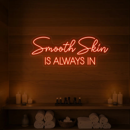 Photo of the 'Smooth Skin Is Always In' neon sign glowing in golden yellow against a styled interior wall.
