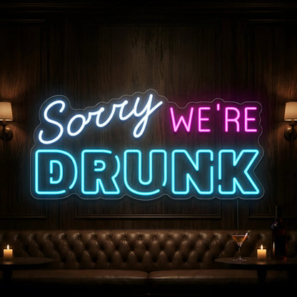 Photo of the 'Sorry We’re Drunk' neon sign glowing in multi-color against a fun bar-inspired wall.