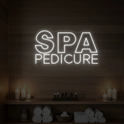 Photo of the 'Spa Pedicure' neon sign glowing in cool white against a styled interior wall.