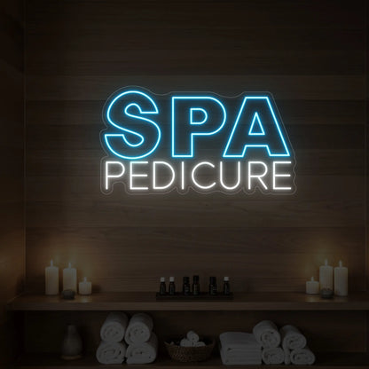 Photo of the 'Spa Pedicure' neon sign glowing in ice blue against a styled interior wall.