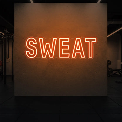  'SWEAT' neon sign glowing in golden yellow against a styled interior wall.