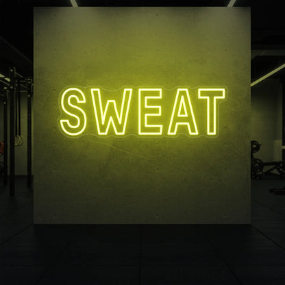  'SWEAT' neon sign glowing in lemon yellow against a styled interior wall.