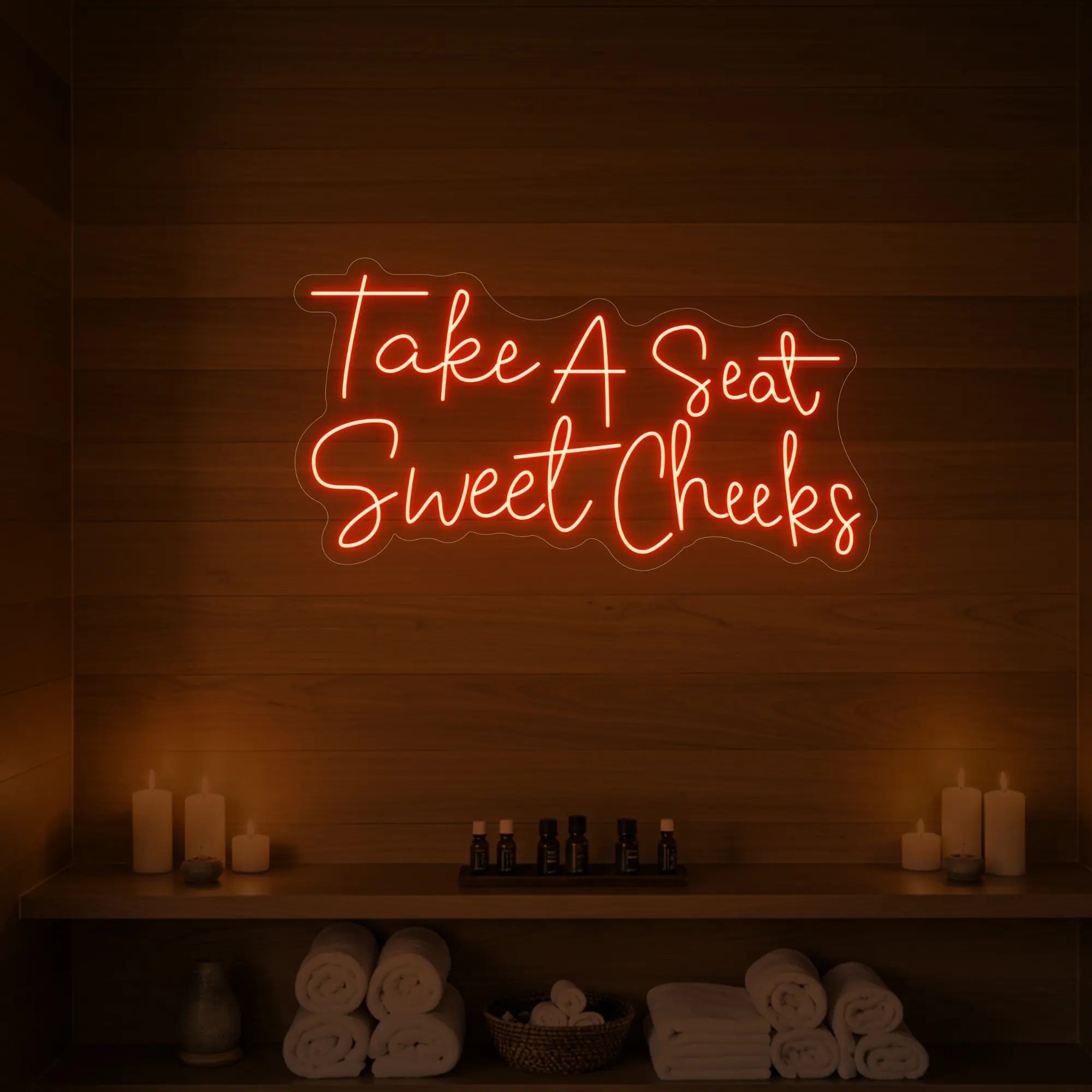 Photo of the 'Take A Seat Sweet Cheeks' neon sign glowing in golden yellow against a styled interior wall.