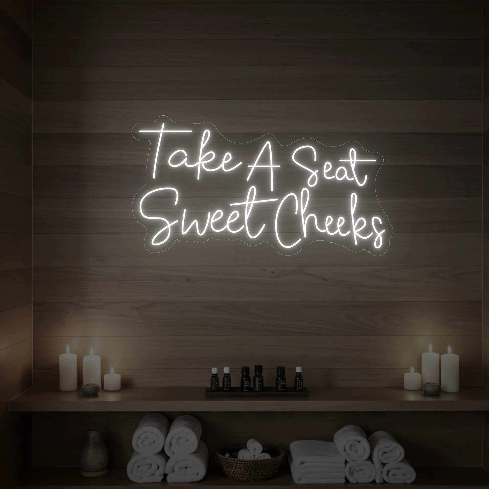 Photo of the 'Take A Seat Sweet Cheeks' neon sign glowing in warm white against a styled interior wall.