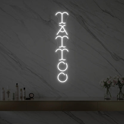 Photo of the 'Vertical Tattoo' neon sign glowing in cool white against a styled interior wall.