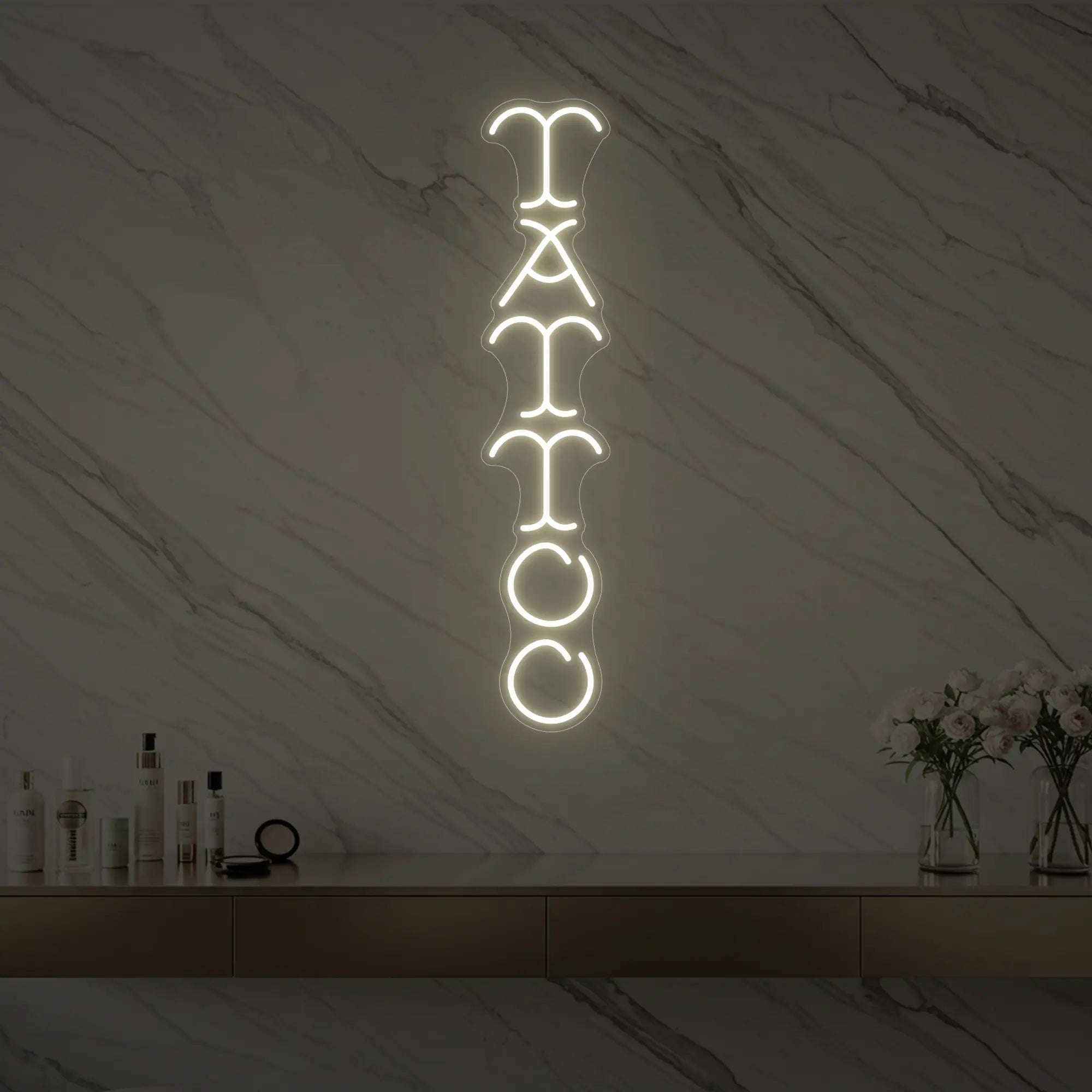 Photo of the 'Vertical Tattoo' neon sign glowing in warm white against a styled interior wall.