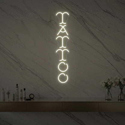 Photo of the 'Vertical Tattoo' neon sign glowing in warm white against a styled interior wall.