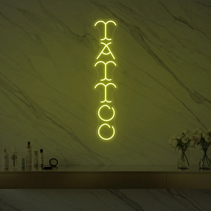Photo of the 'Vertical Tattoo' neon sign glowing in lemon yellow against a styled interior wall.