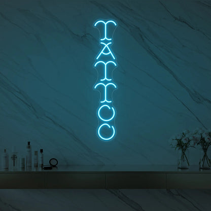 Photo of the 'Vertical Tattoo' neon sign glowing in ice blue against a styled interior wall.