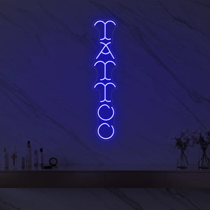 Photo of the 'Vertical Tattoo' neon sign glowing in deep blue against a styled interior wall.
