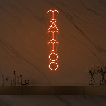 Photo of the 'Vertical Tattoo' neon sign glowing in golden yellow against a styled interior wall.