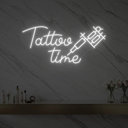 Photo of the 'Tattoo Time' neon sign glowing in cool white against a styled interior wall.