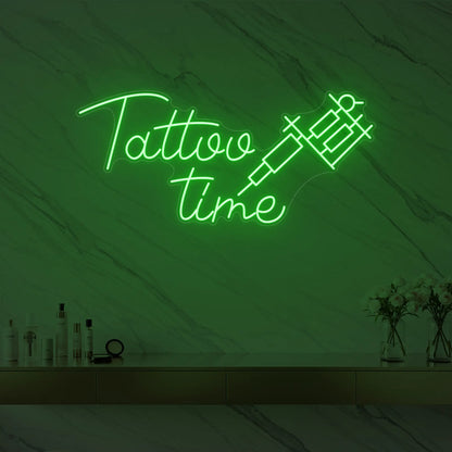 Photo of the 'Tattoo Time' neon sign glowing in green against a styled interior wall.