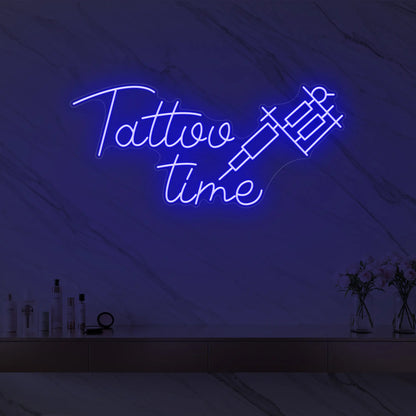Photo of the 'Tattoo Time' neon sign glowing in deep blue against a styled interior wall.