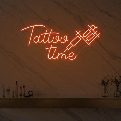 Photo of the 'Tattoo Time' neon sign glowing in golden yellow against a styled interior wall.