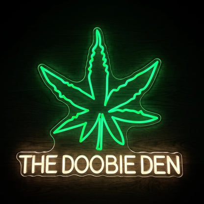The Doobie Den LED neon sign on clear acrylic backing with a green cannabis leaf and warm white lettering for cannabis-themed wall décor.